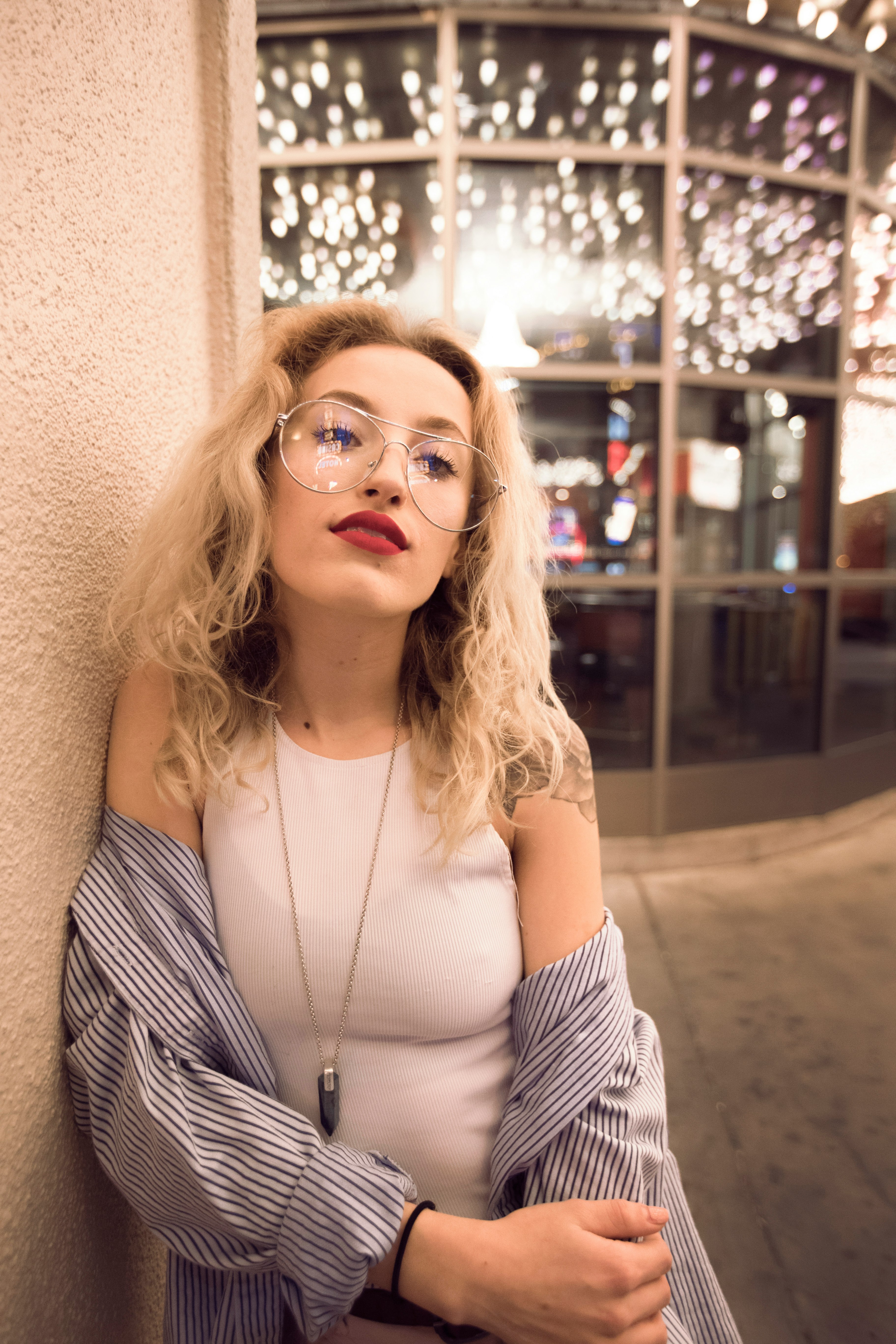 woman leaning on white painted concrete wall wearing white sleeveless top with white and black striped long-sleeved shirt